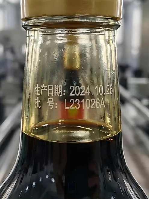 Two lines of print on the shoulder of a glass bottle: the production date above, the batch number below