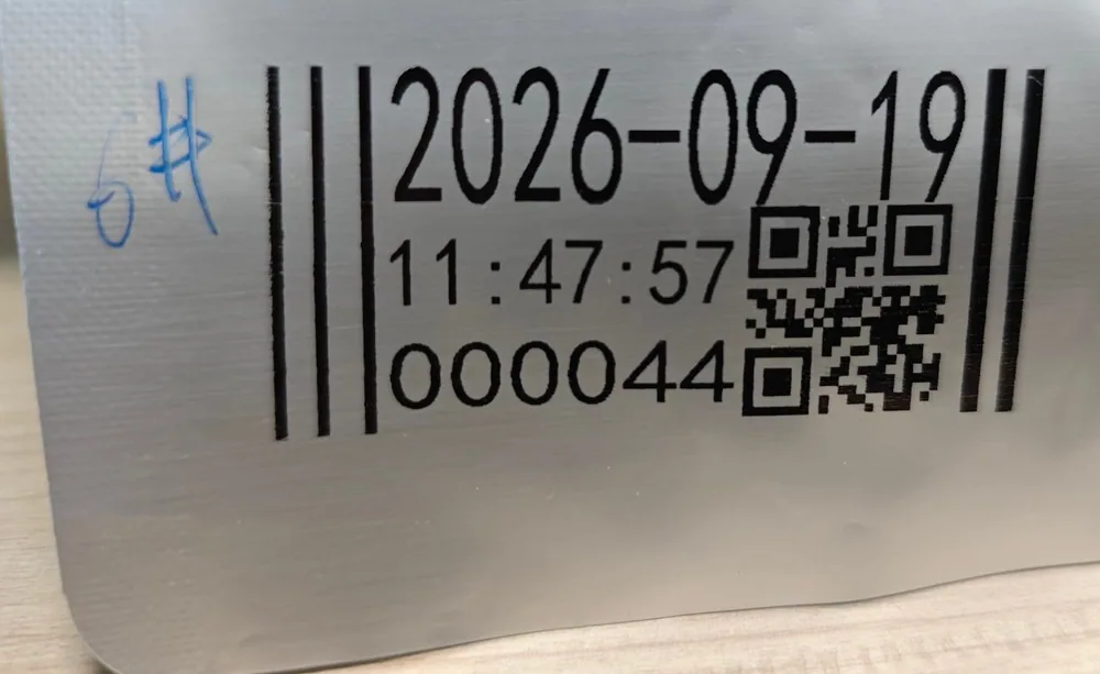 Several codes printed across a plain silver aluminium foil pouch, each carrying the wordmark, a 2D code, a running number and a time